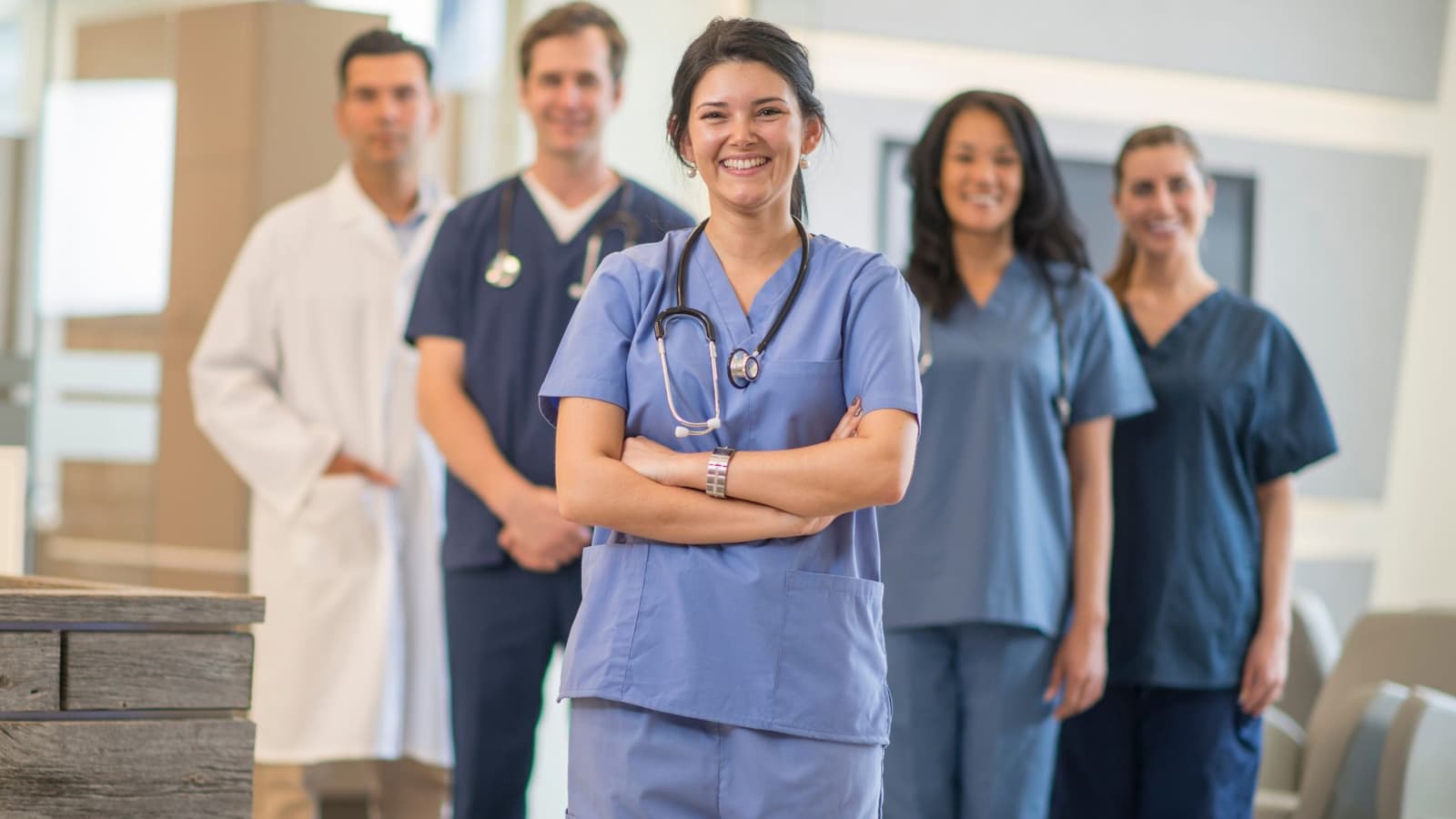 A smiling nurse in scrubs standing in front of her healthcare team
