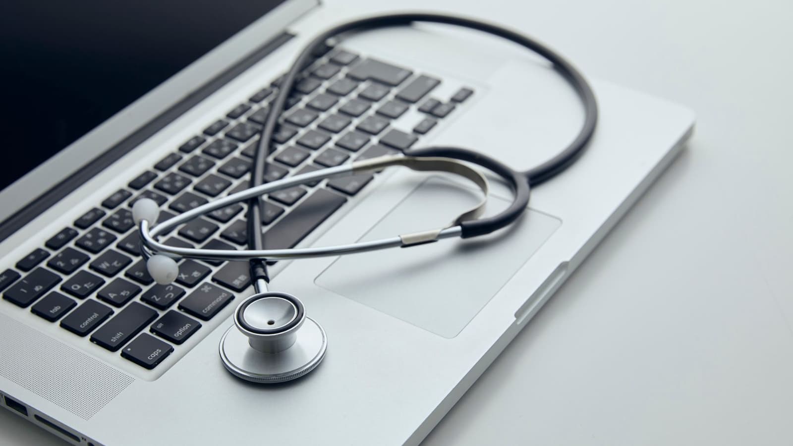 A stethoscope resting beside an open laptop on a desk